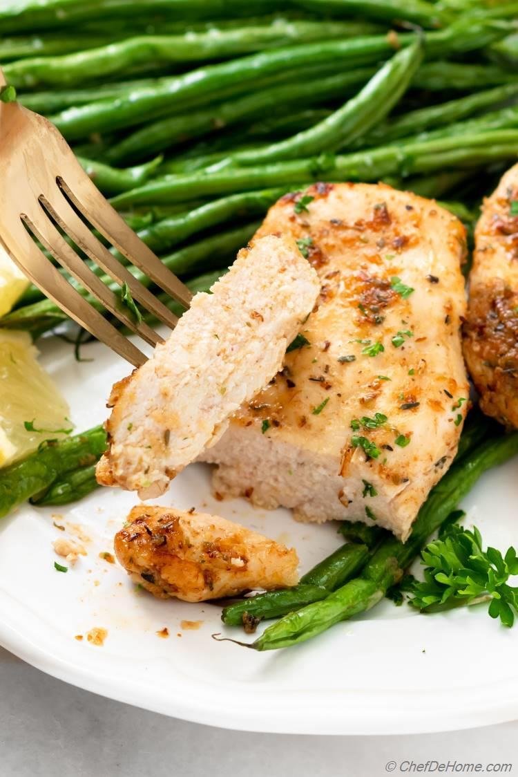 Herb-seasoned chicken breast sliced on a plate with green asparagus and a lemon wedge nearby.