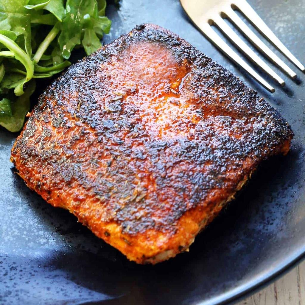 Crispy, well-seared salmon fillet on a dark plate with a side of greens and a fork nearby