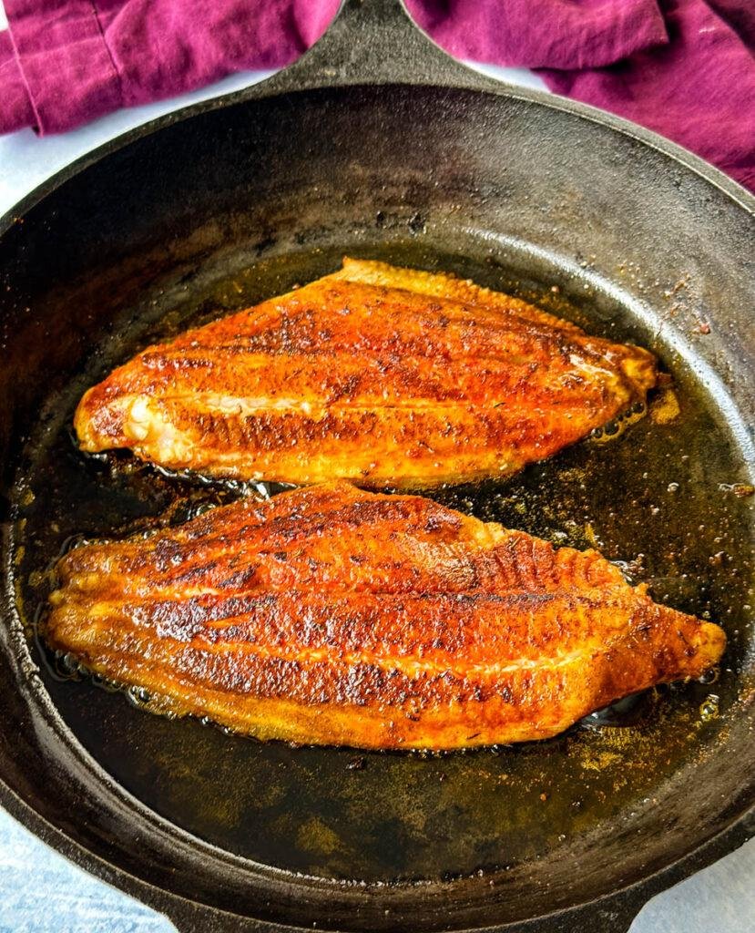 Two pan-seared salmon fillets browning in a cast-iron skillet with crispy skin and golden crusts.