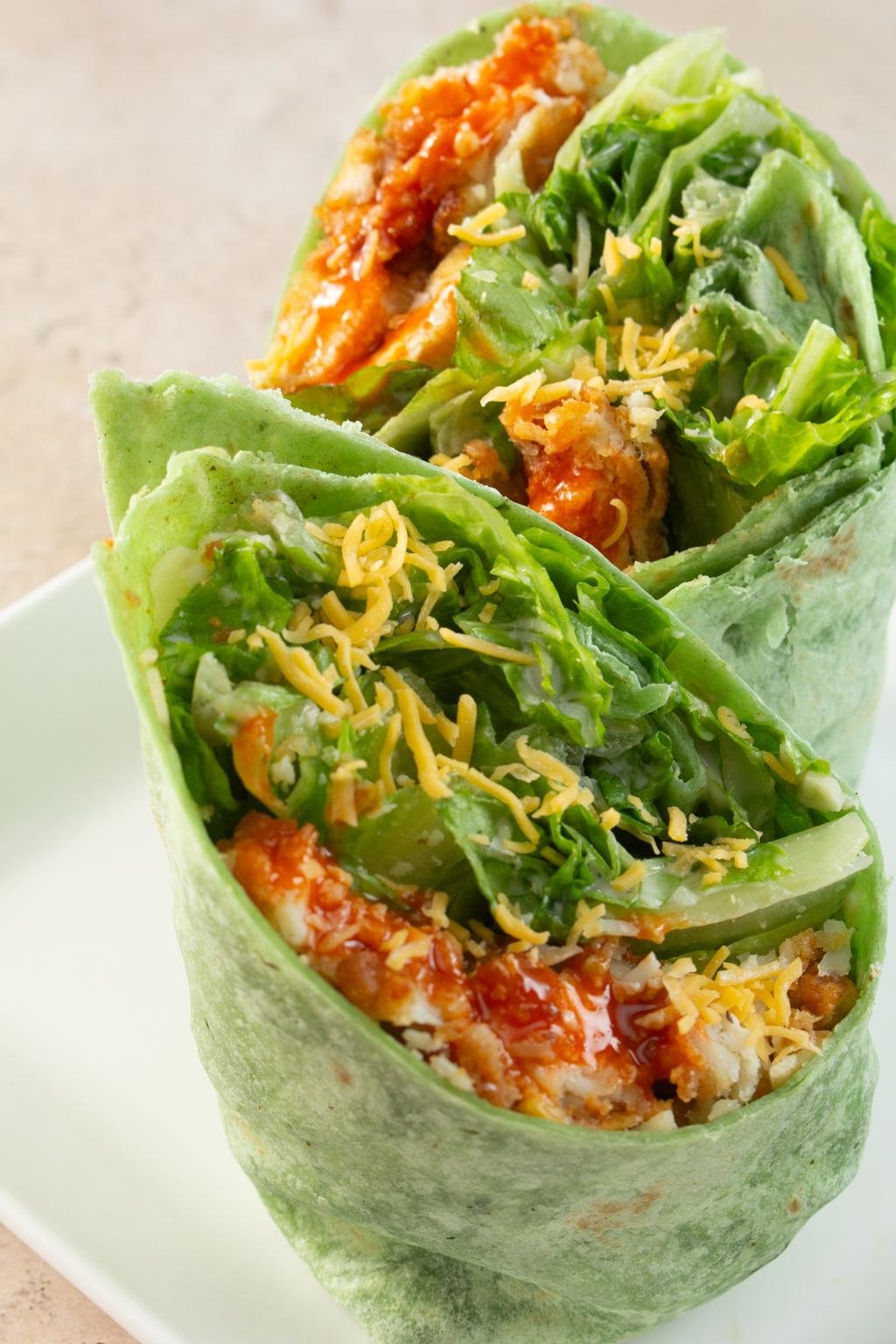 Spinach tortilla wraps filled with lettuce, chicken, salsa, and shredded cheese on a white plate moment.