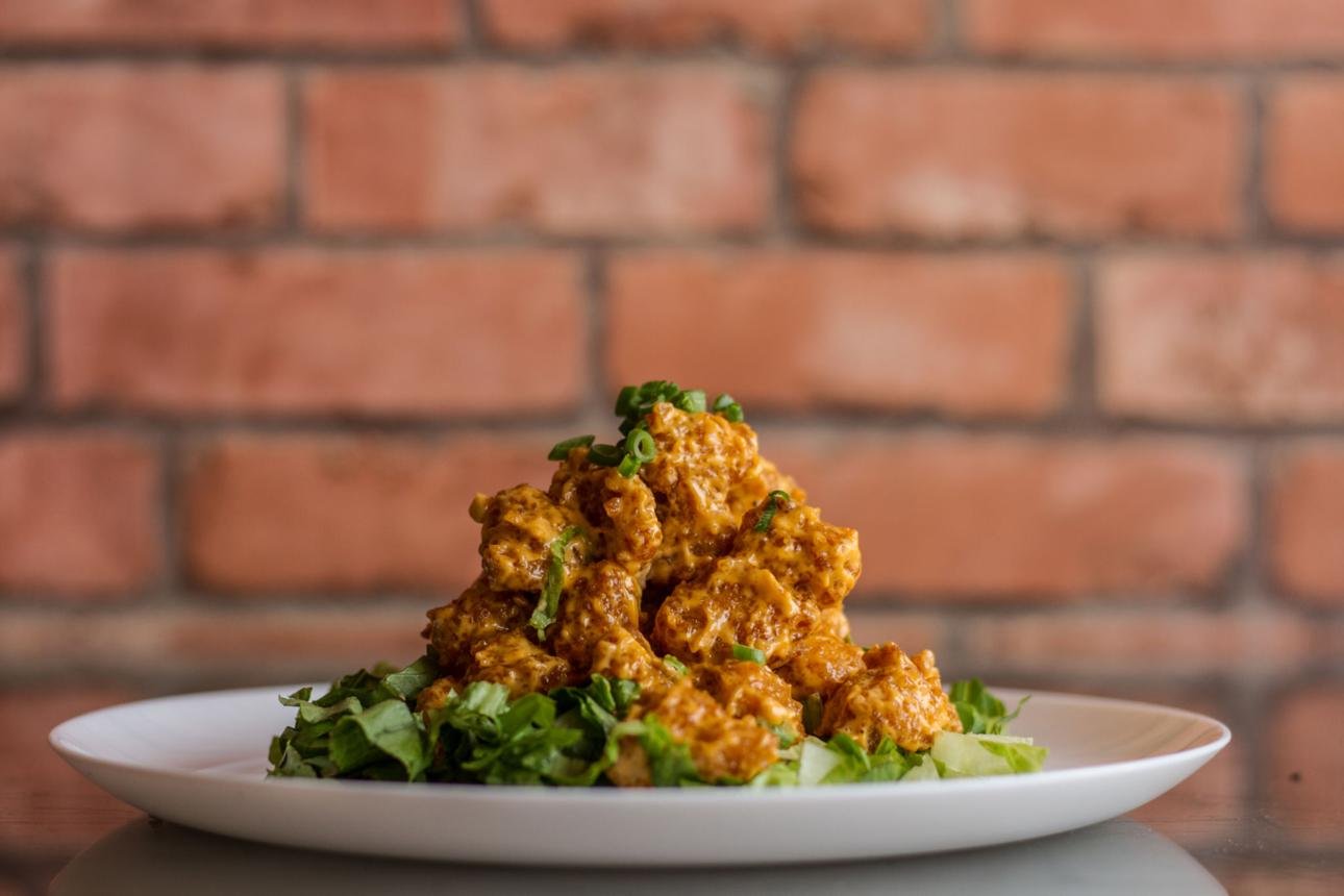 Spicy fried chicken bites piled on a bed of chopped greens on a white plate, with a brick wall background.