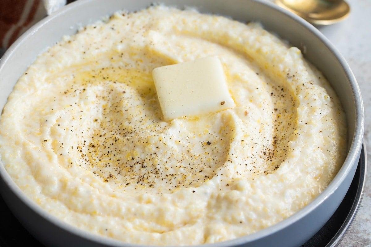 Creamy mashed potatoes in a pan topped with a pat of melting butter and a sprinkle of black pepper.