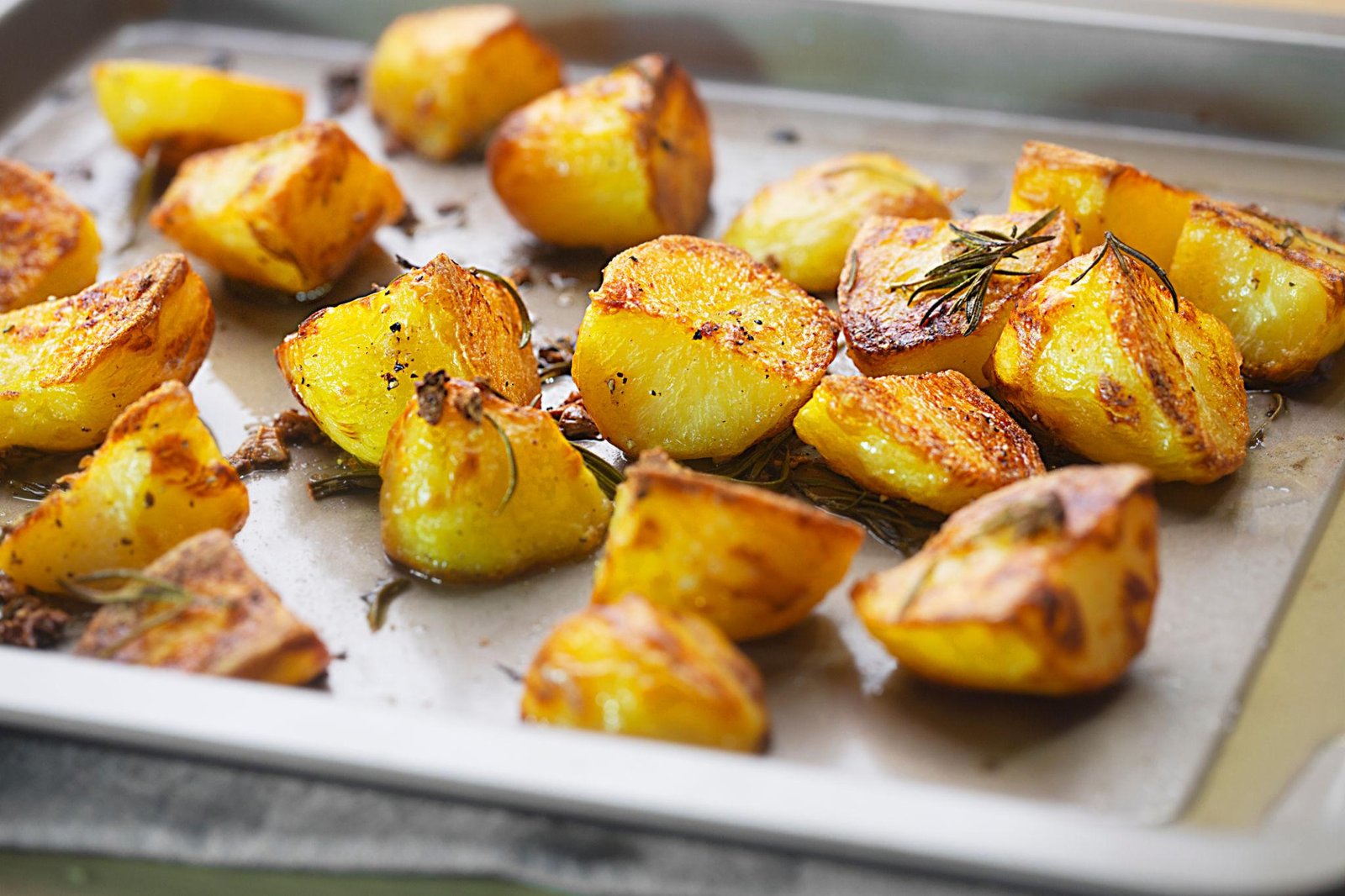 Golden brown roasted potato wedges on a baking sheet with rosemary sprigs.