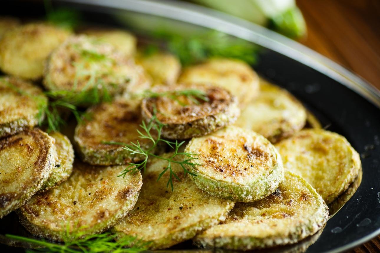 Breaded zucchini rounds fried in a skillet with fresh dill garnish