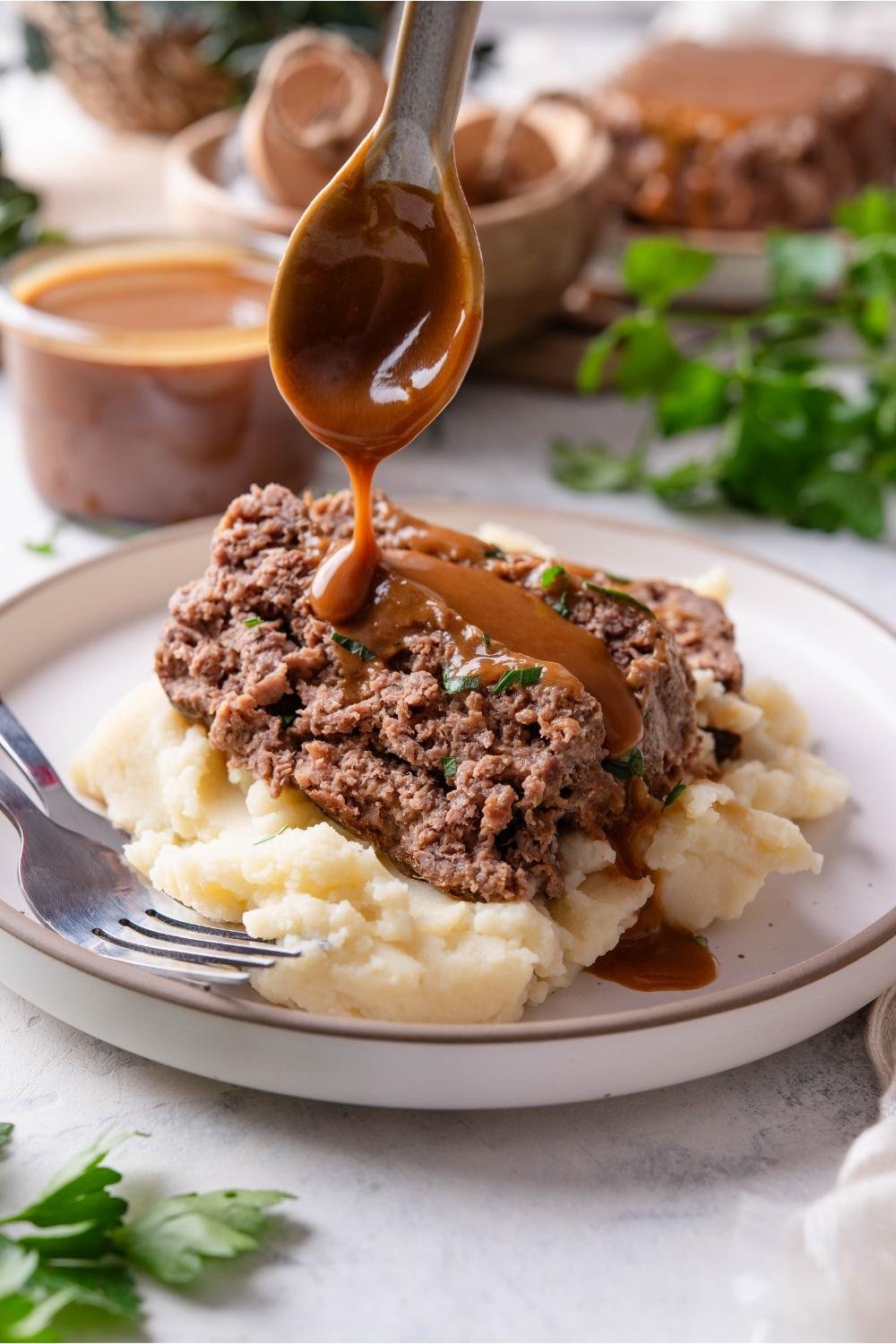 Plate of mashed potatoes topped with a beef patty and brown gravy being poured over it.