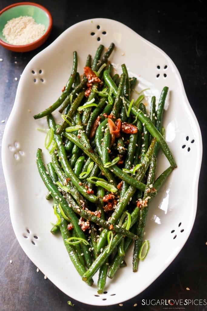 Sautéed green beans garnished with sesame seeds, chili, and sliced scallions on a white platter.