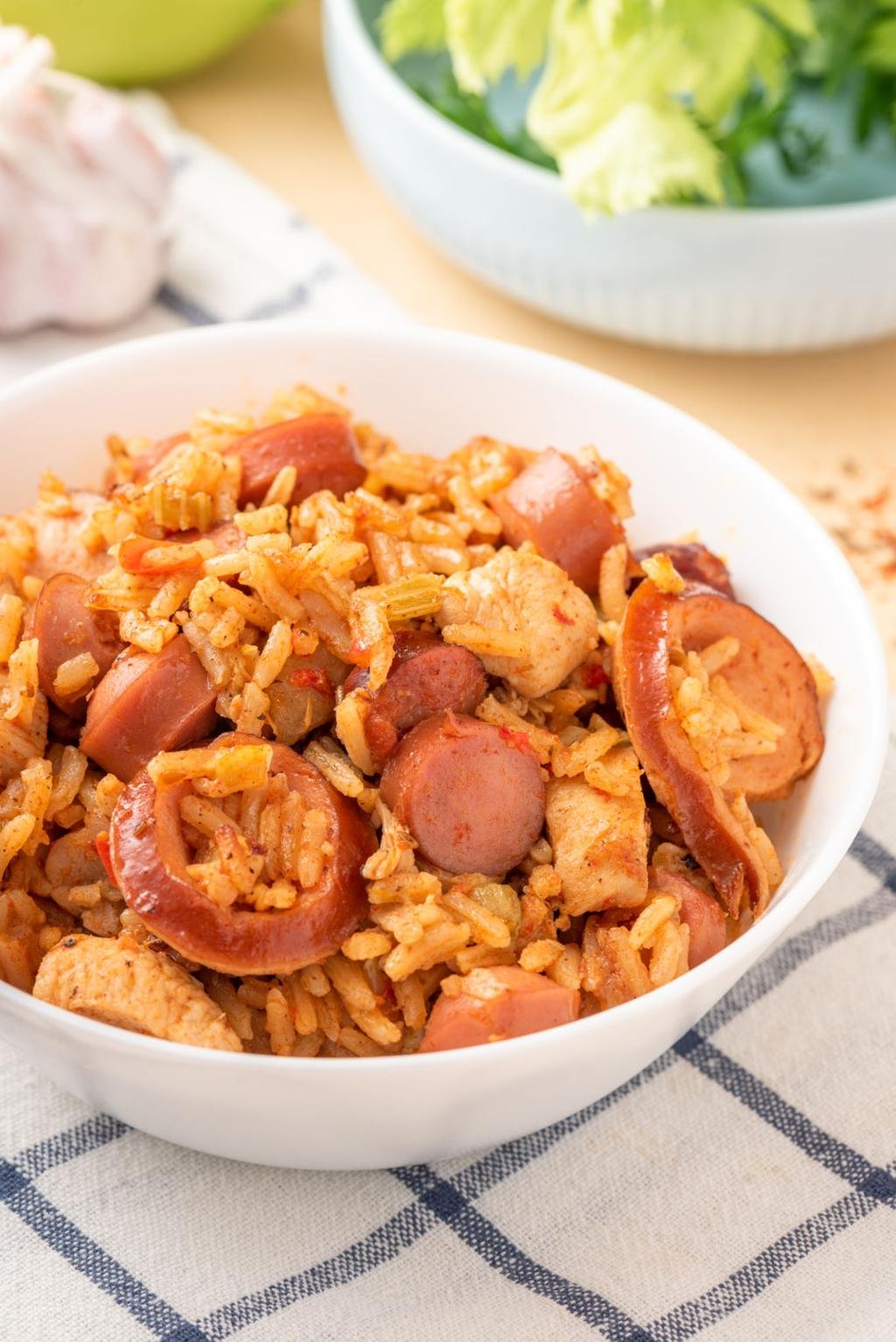 Bowl of sausage and rice dish with sliced sausage pieces on a white bowl, resting on a checkered cloth.