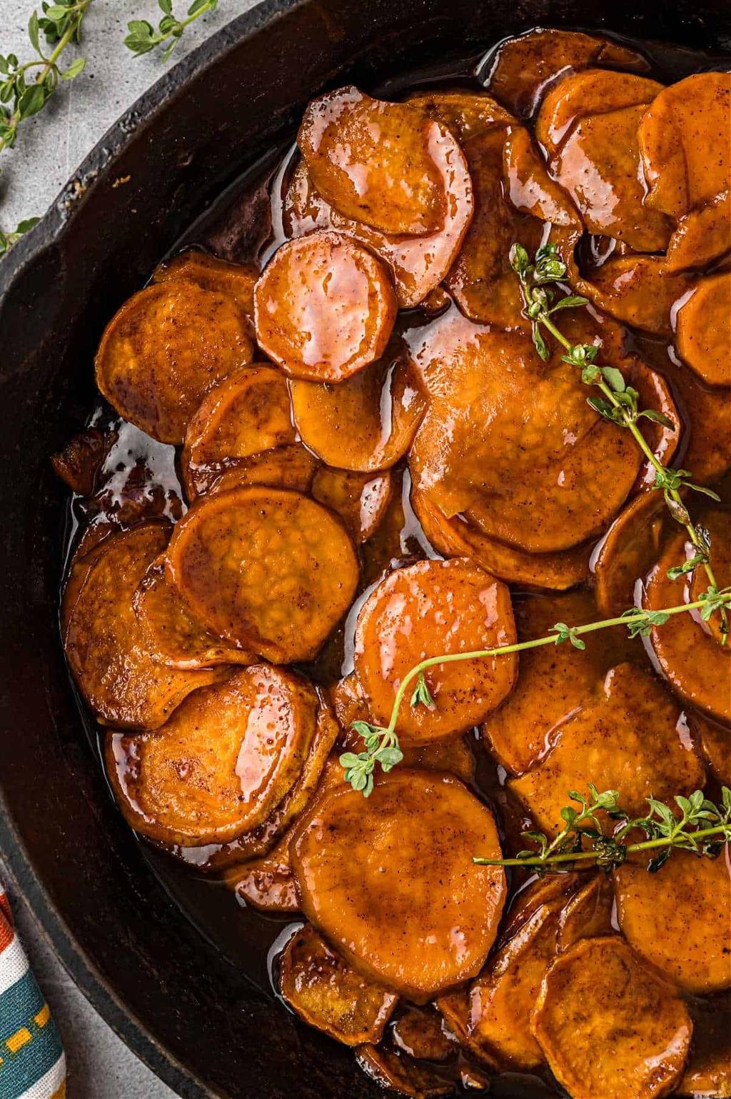Sliced sweet potatoes glazed in a glossy brown sauce simmering in a cast iron skillet with thyme sprigs