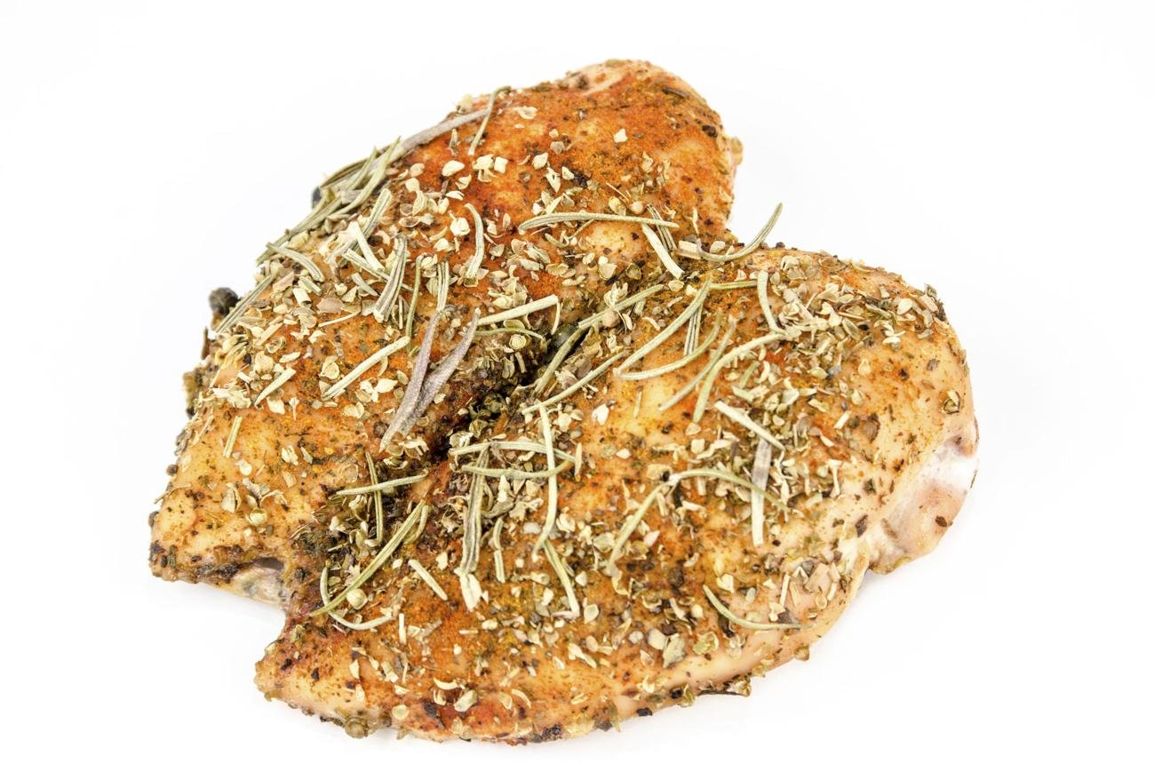 Herb-crusted roasted chicken thighs on a white background, sprinkled with rosemary and oregano.