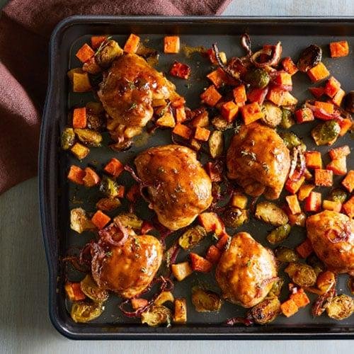 Baked meatballs on a dark baking sheet surrounded by roasted potatoes, carrots, peppers, and onions cut into small cubes.