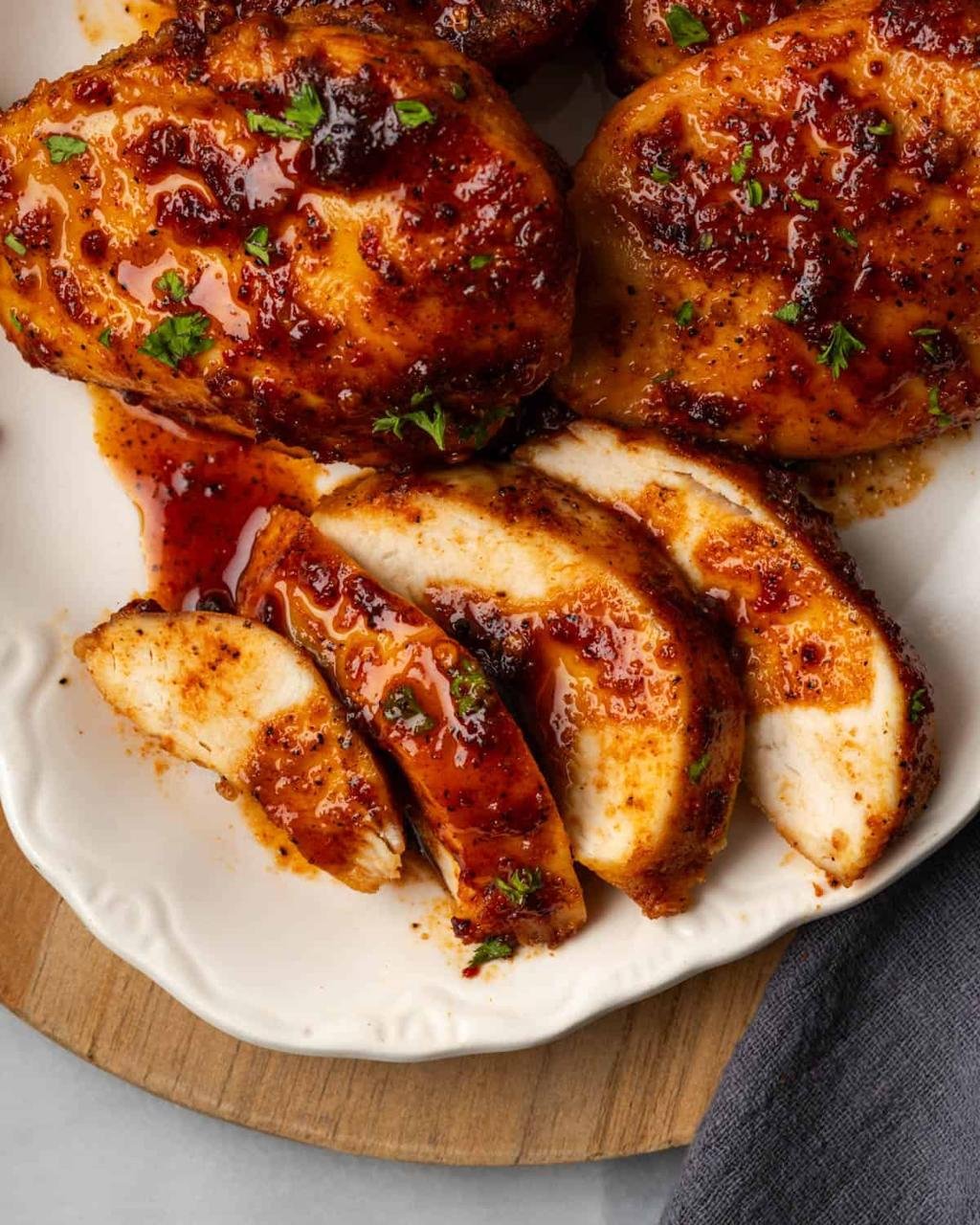 Plate of glossy, herb-garnished glazed chicken pieces with a reddish-brown sauce on a white platter