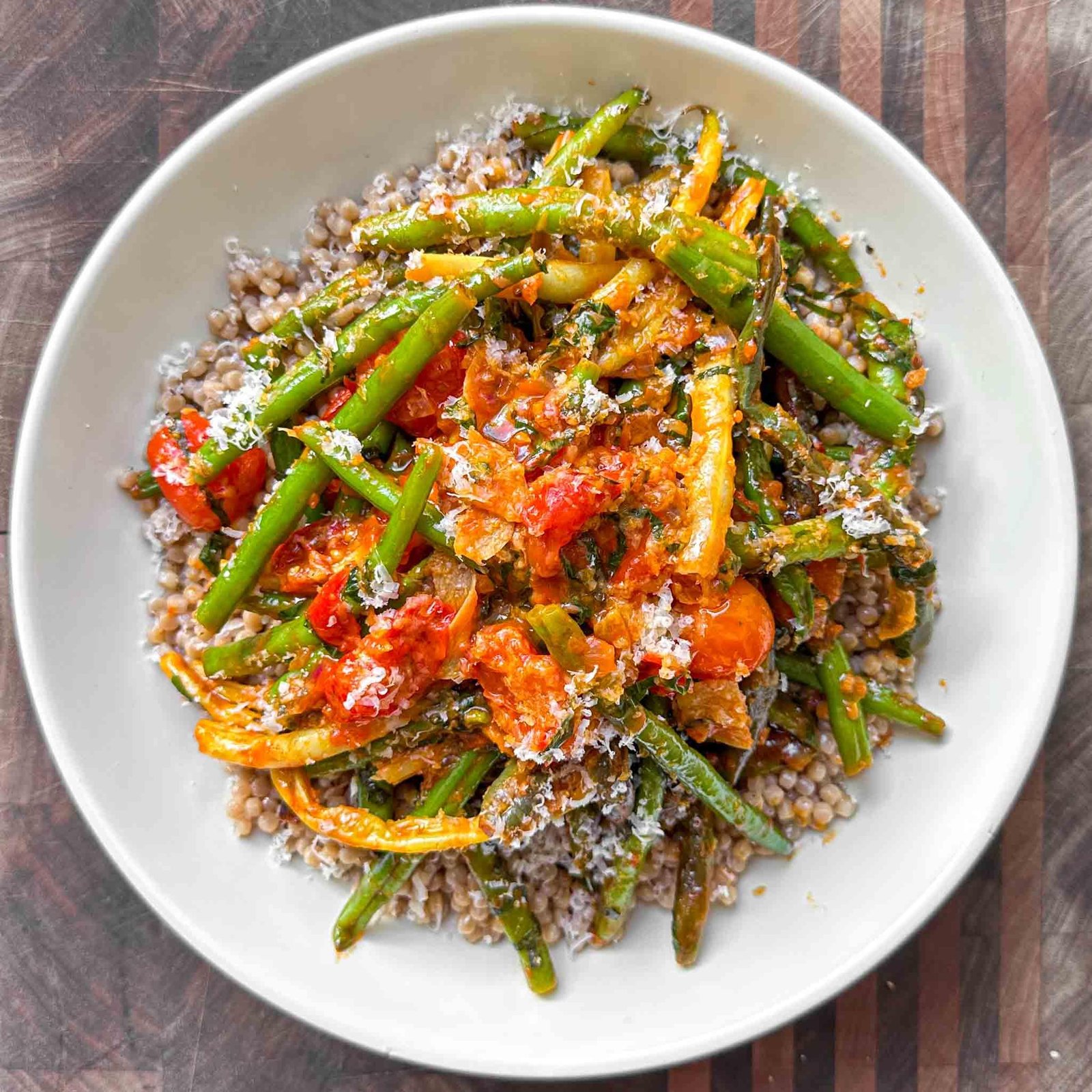 Plate of lentils topped with sautéed green beans and colorful vegetables, finished with grated cheese on top.