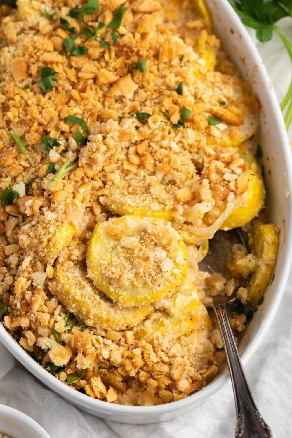 Oval baking dish filled with peach crumble, golden crumb topping and a hint of green herb garnish.