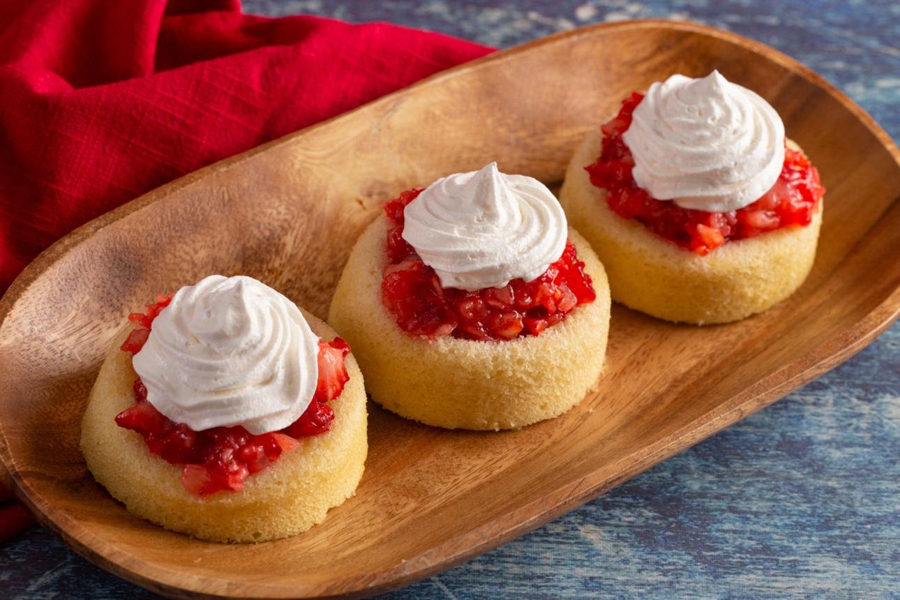 Three vanilla cupcakes with strawberry jam centers and white whipped-cream swirls on a wooden platter.